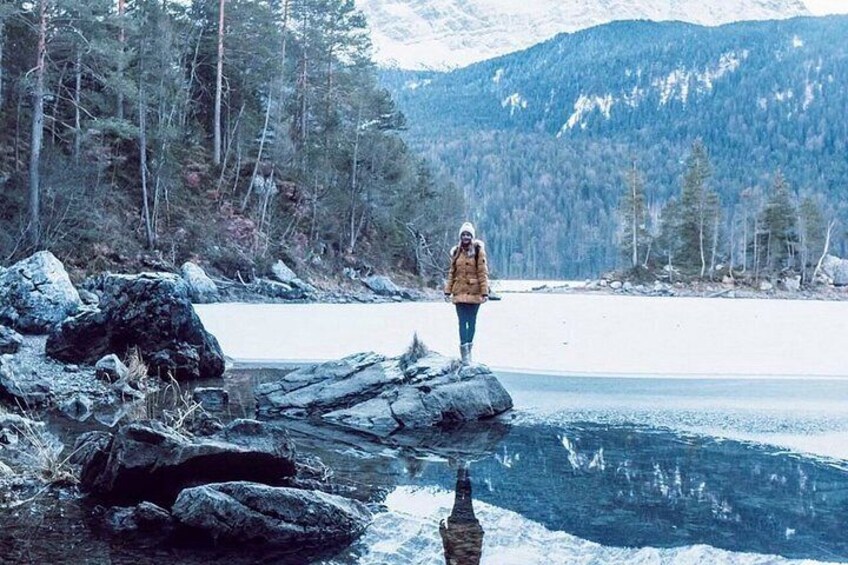 A person standing on rocks by a frozen lake with snow-covered mountains in the background. 2