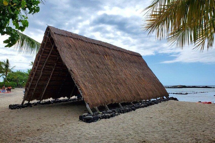 A thatched-roof structure on a sandy beach with palm trees and the ocean in the background. 2