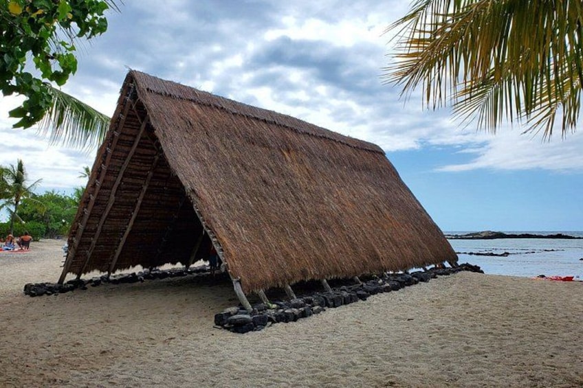 Una estructura con techo de paja en una playa arenosa, con palmeras y el océano al fondo. 4