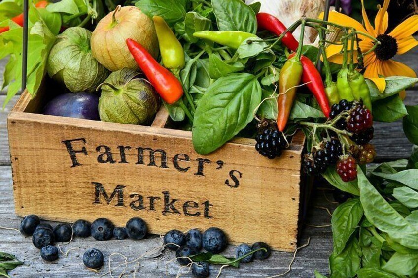 Una caja de madera con la etiqueta 'Farmer's Market' llena de diversos productos frescos como tomates, pimientos y verduras de hoja. 1