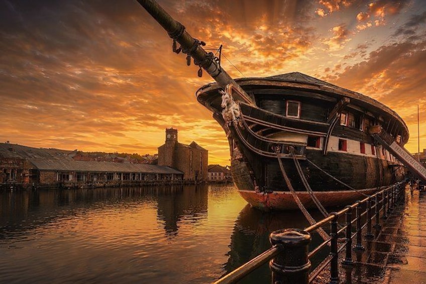 A historic ship docked at a pier during sunset. 1