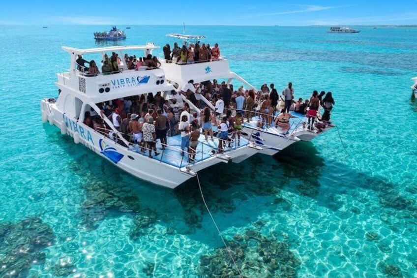 A boat with 'VIBRA' written on it, surrounded by clear turquoise water and visible underwater rocks. 2