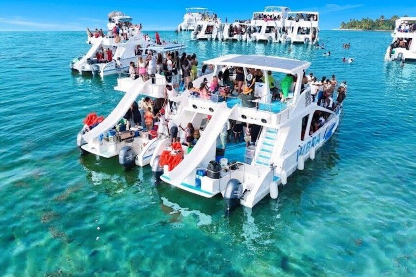 A group of white boats with people on them, floating on clear blue water. 3