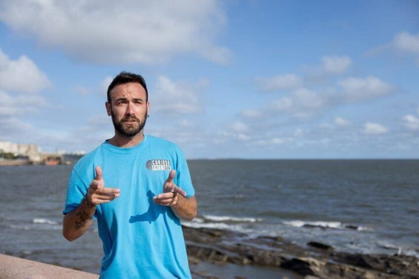 A person in a blue shirt gesturing by the sea. 5