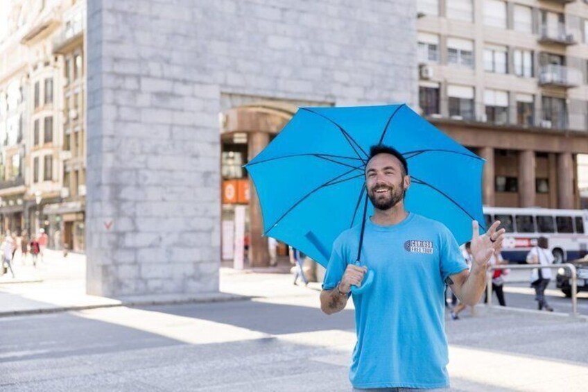 A person holding a blue umbrella in an urban setting with buildings and a bus in the background. 4