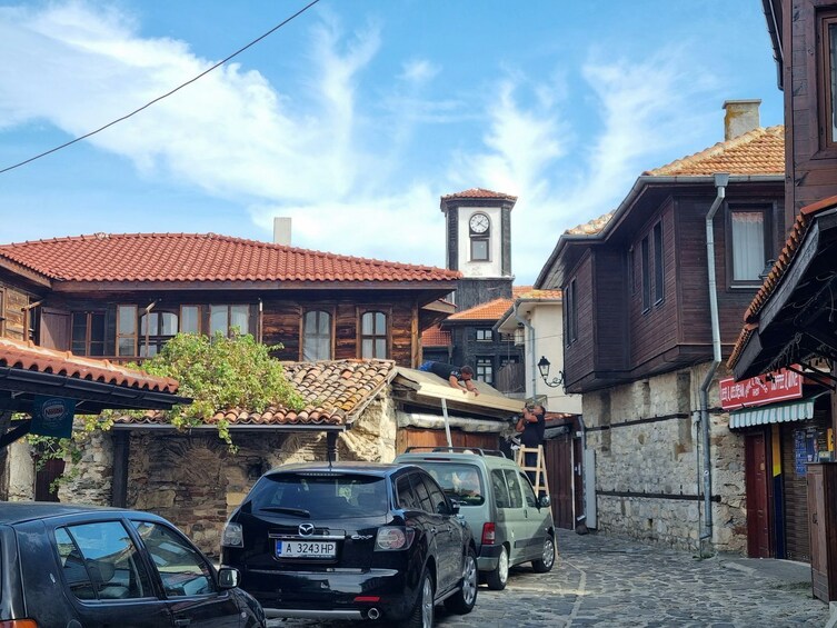 A narrow street with traditional buildings, a clock tower, and parked cars. 4