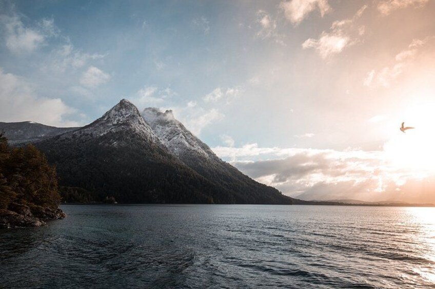 A mountain with a lake in the foreground and a bird flying in the sky. 4