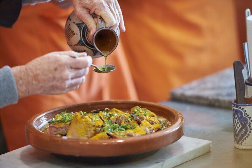 An elderly person pouring sauce into a dish with meat and vegetables. 1