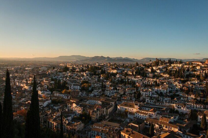 A cityscape at dusk with buildings, a prominent church spire, and distant mountains. 4