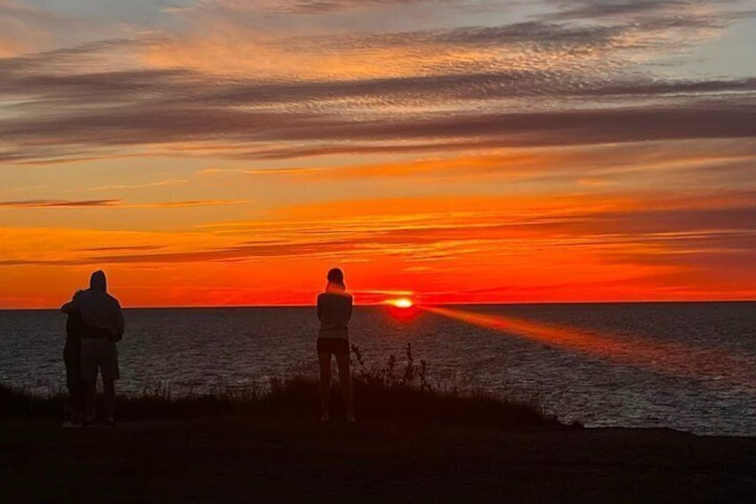 A sunset over the ocean with two silhouetted figures on a beach. 5