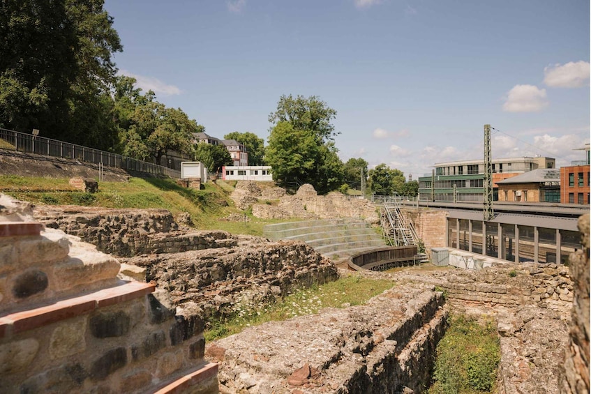 Ancient ruins with stone structures and a modern building in the background. 1