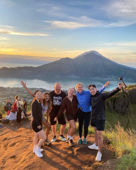 A group of people posing on a mountain overlook with a volcano in the background. 3