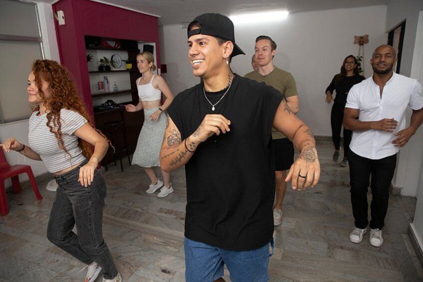 A group of people dancing in a room with a red chair and a whiteboard in the background. 1