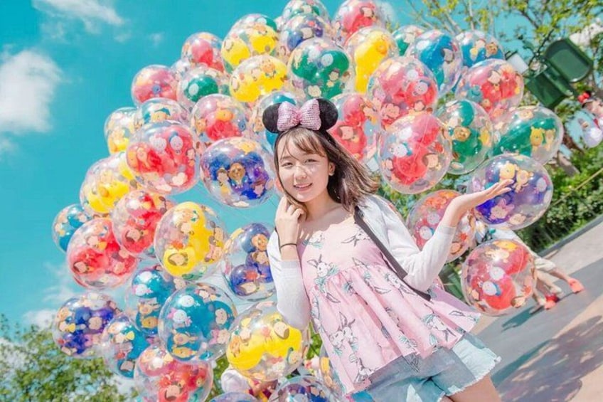 A person standing in front of a cluster of colorful balloons with cartoon characters. 5