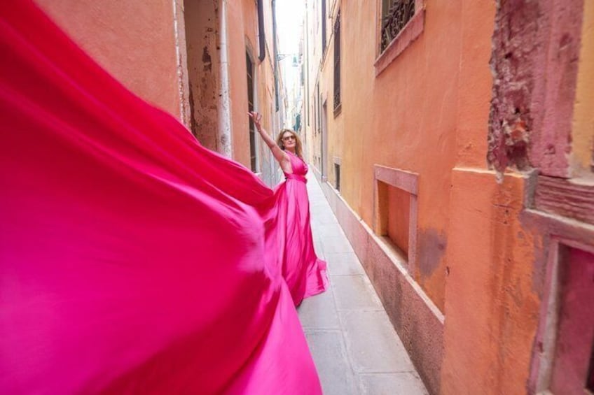 A person in a pink dress walking down a narrow street with buildings on either side. 2