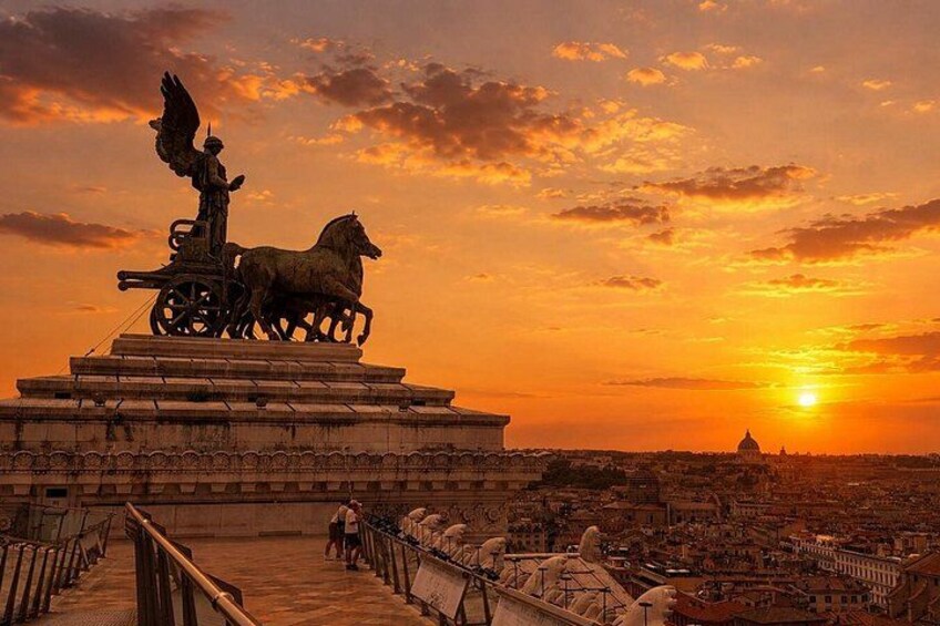 Un coucher de soleil sur une ville, avec une statue d’un ange sur un char tiré par des chevaux, un pont et, au loin, une structure en forme de dôme. 1