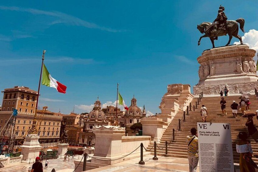Un monument historique surmonté d’une statue, avec un escalier menant à sa base et des drapeaux flottant au vent. 5