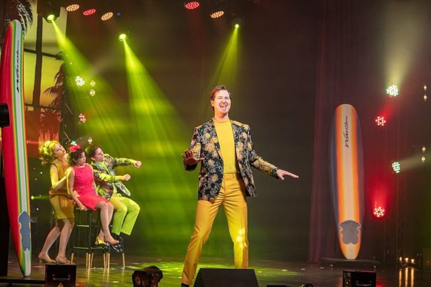 A stage with a performer in yellow, a large pencil prop, and stage lighting. 5