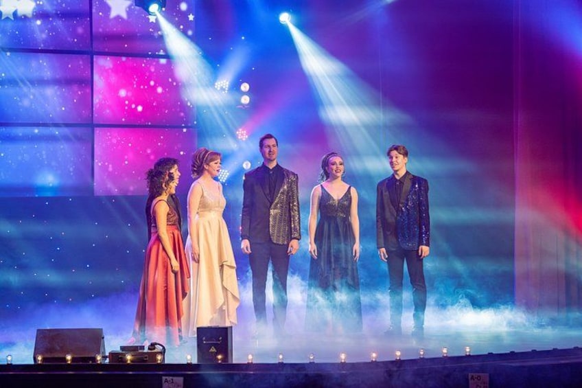 A stage with five people standing, a large screen in the background, and stage lights. 4