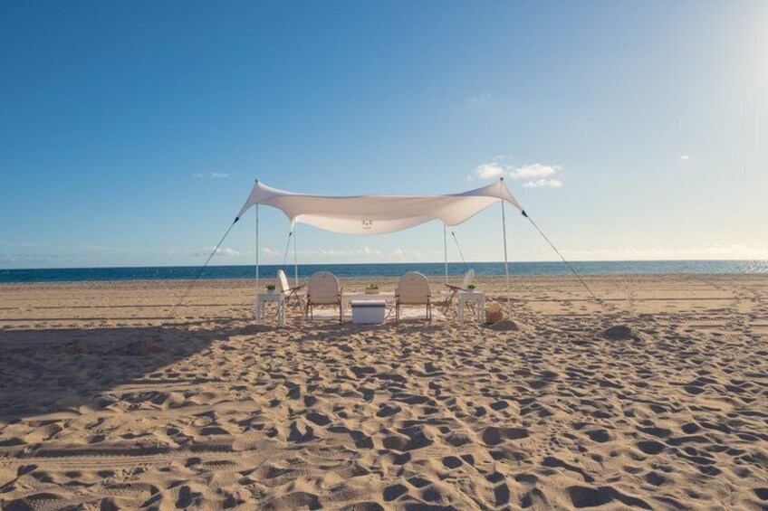 A beach with a white canopy tent, two chairs, and a table. 3