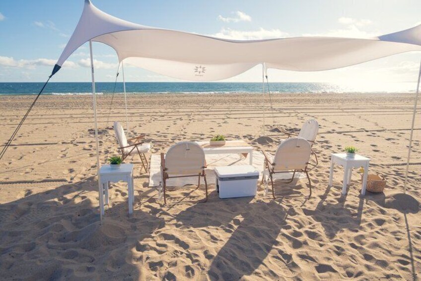 A beach setting with a canopy, lounge chairs, a table, and a cooler. 1