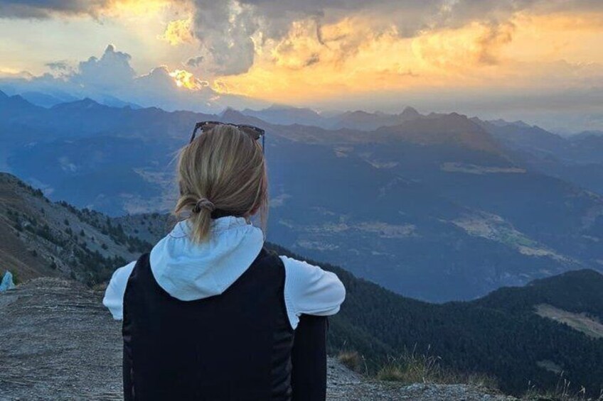 A person standing on a mountain ridge overlooking a valley with a sunset in the background. 3