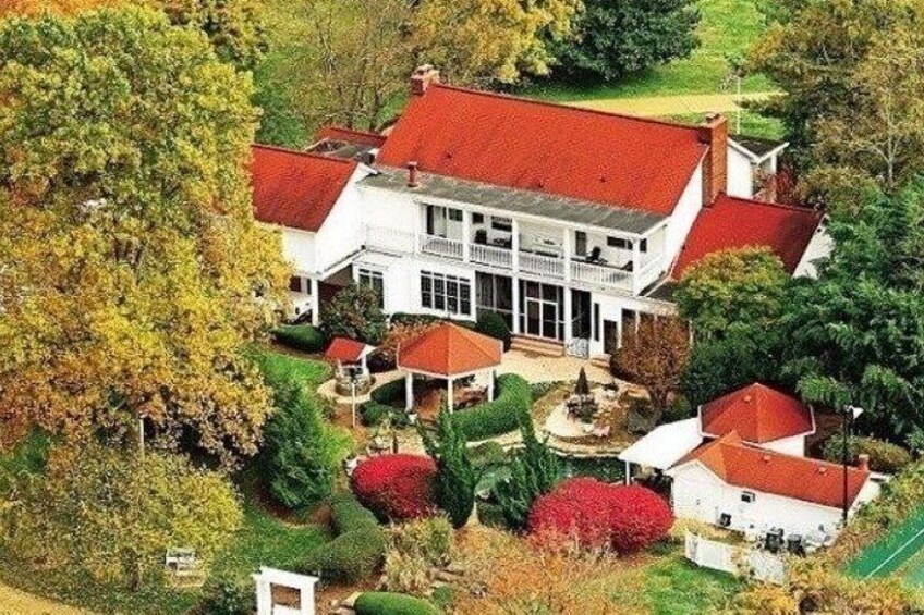 A large white house with a red roof, surrounded by trees and shrubs. 5