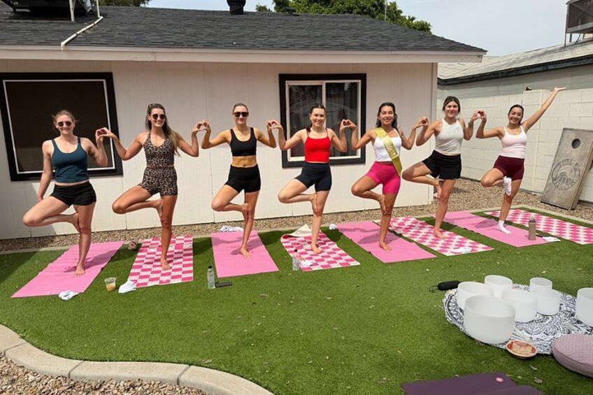 A group of people performing yoga on mats in an outdoor setting with a house in the background. 1