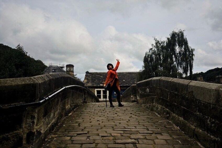 A person walking on a stone bridge with a railing, surrounded by trees and buildings. 1
