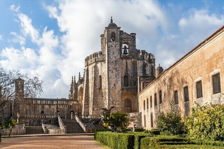 A historic stone building with a bell tower, a staircase, and a well-maintained garden. 3