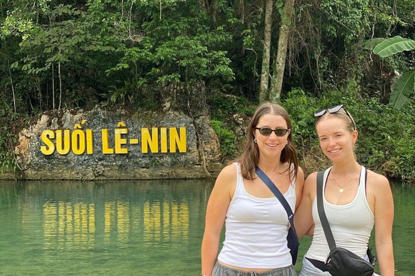 Two people standing by a body of water with a rocky outcrop in the background and the text 'SUOI LÊ-NIN' visible. 2