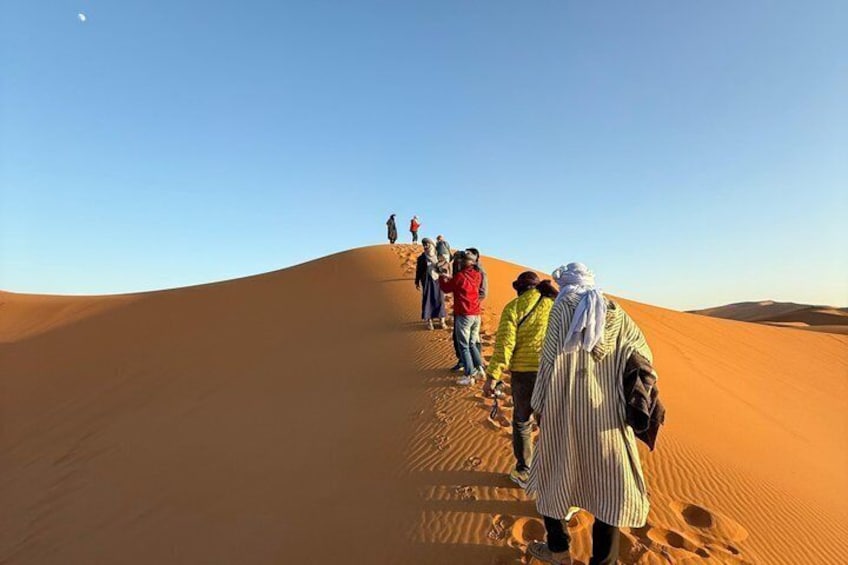 A group of people hiking on a sand dune under a clear sky. 1