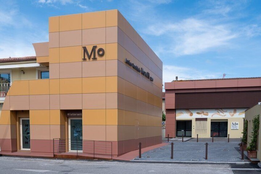 A modern building with the 'Mo' logo, a restaurant sign, and a clear sky. 3