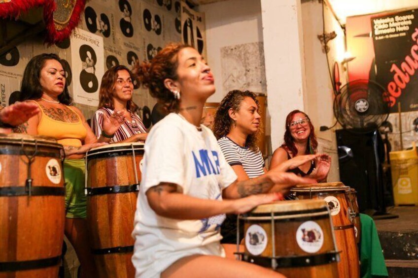 A group of people playing drums in a room with posters on the wall. 3