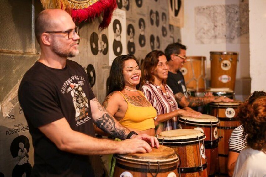 A group of people playing drums in a room with posters on the wall. 5