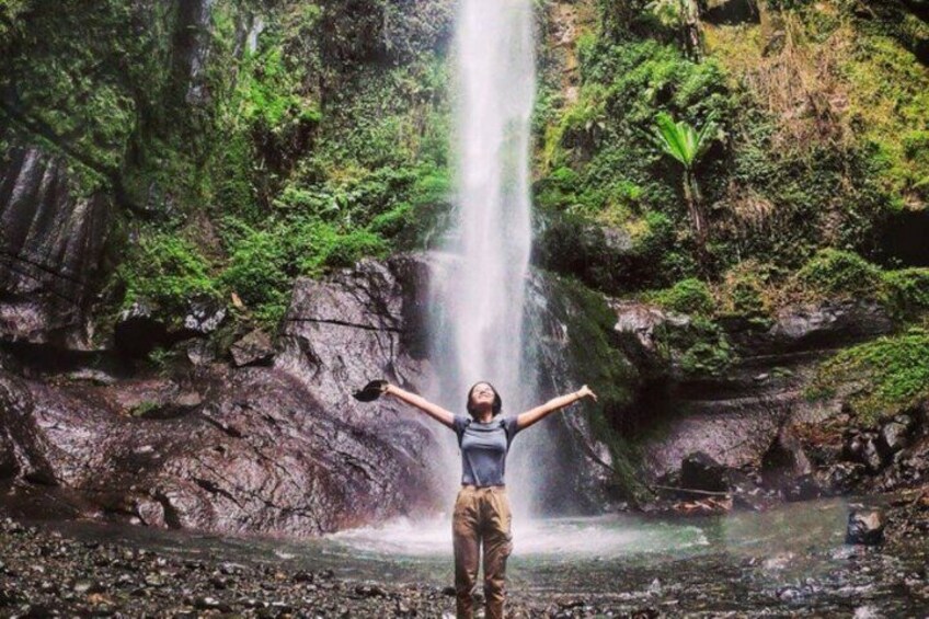A person standing with arms outstretched in front of a waterfall. 1