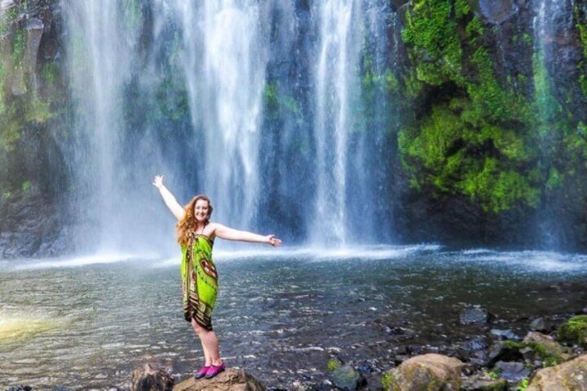 A person standing on a rock with arms outstretched in front of a waterfall. 3