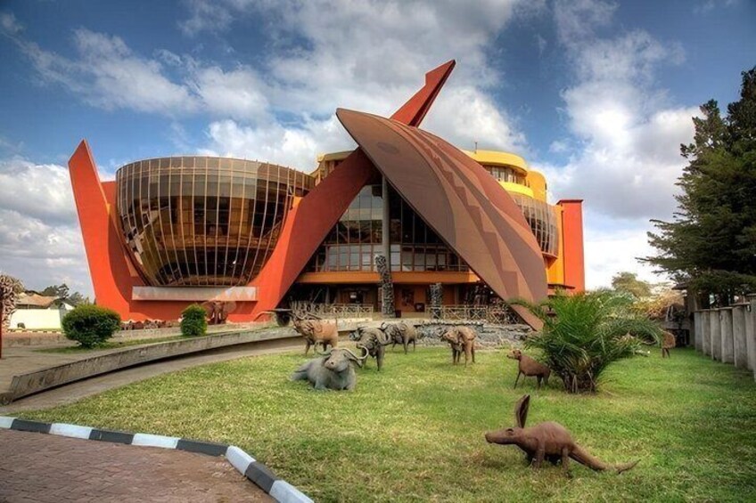 A modern building with a unique curved roof and a large glass facade, surrounded by a well-maintained lawn and various sculptures. 4