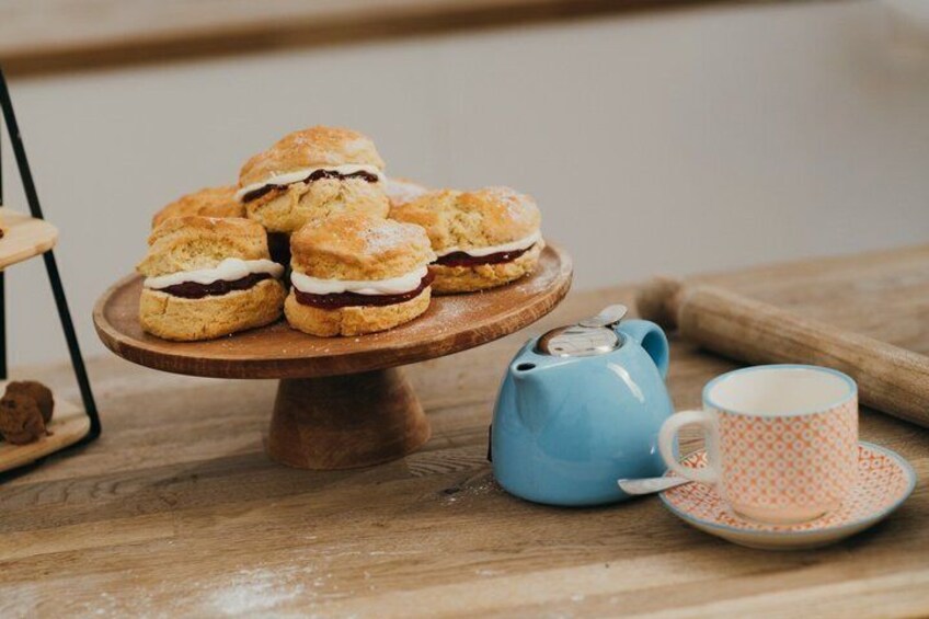 A wooden table with a plate of scones and a teapot. 1