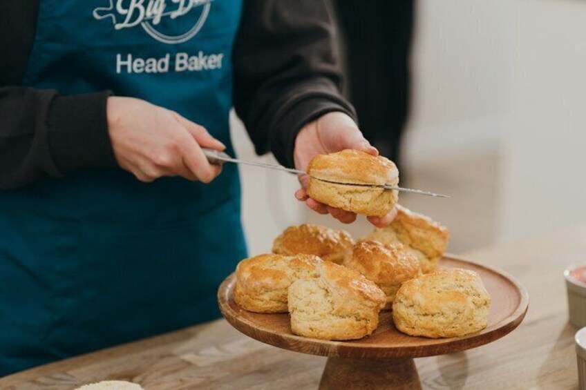 A person in a chef's apron cutting a biscuit on a wooden plate. 5
