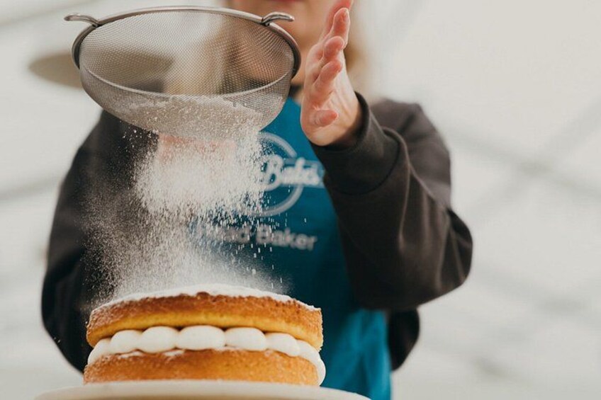 A person in a blue apron sprinkling powdered sugar over a layered dessert. 3
