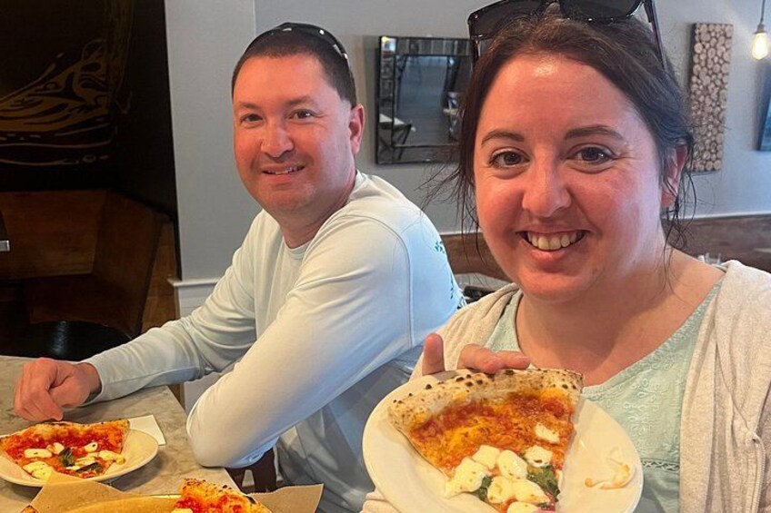 Two people sitting at a table with pizza. 4