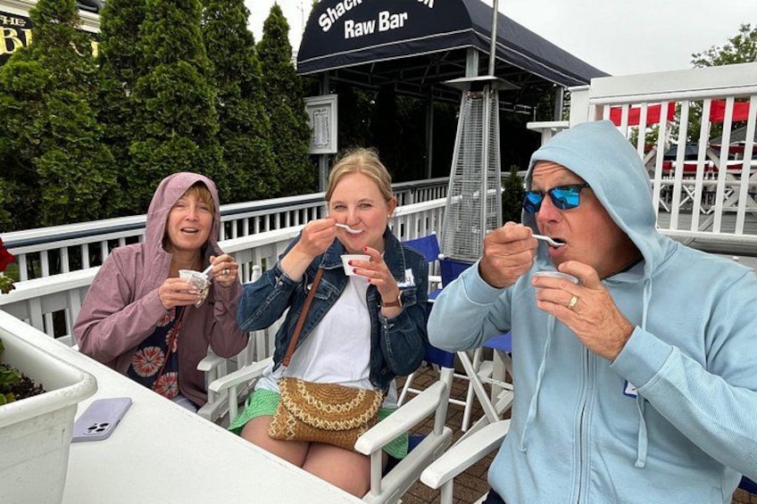 Three people eating at an outdoor event, with a 'Shack Raw Bar' sign in the background. 5