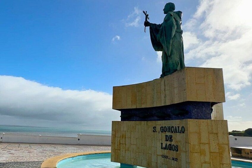A statue of S. Gonzalo de Lagos on a pedestal by a pool with a beach in the background. 4