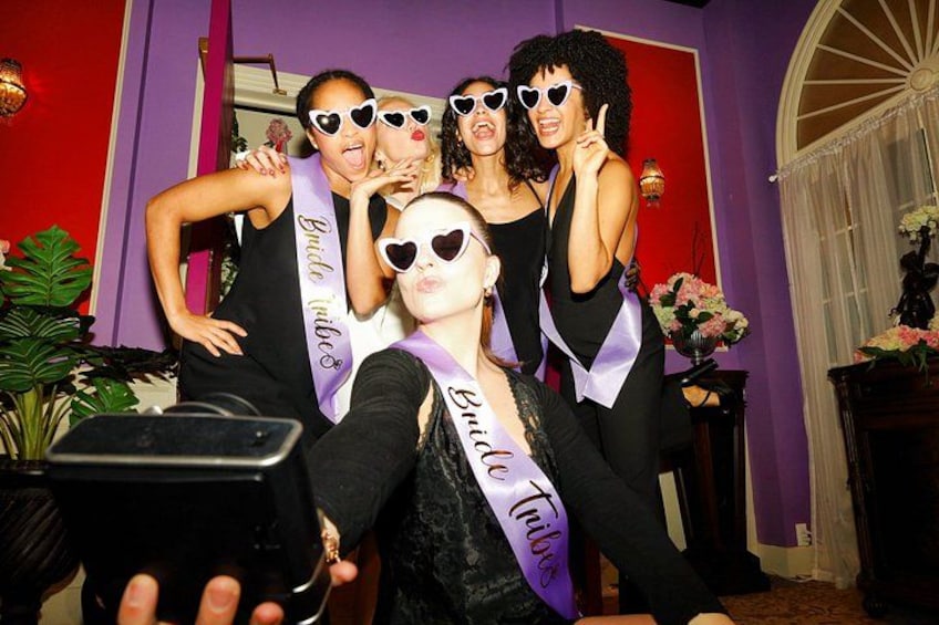A group of people in a room with purple walls, some wearing sashes. 5
