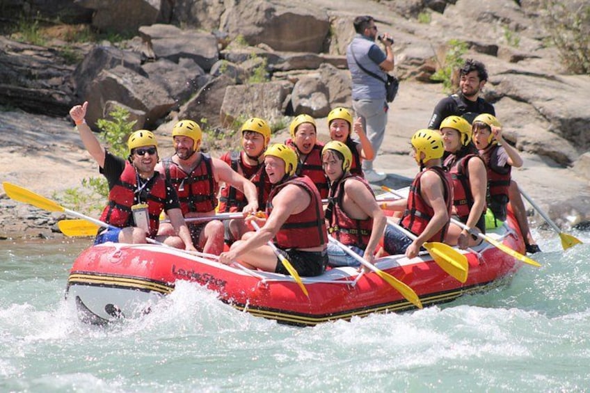 A group of people in a red inflatable raft on a river, wearing helmets and life jackets. 5