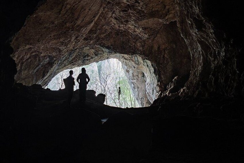 A cave with two people standing inside, looking at a natural light source. 4