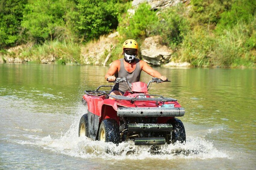 A person riding a red ATV on a river surrounded by greenery. 4