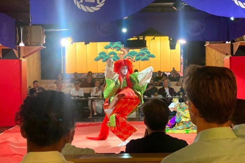 A performer in a colorful costume dancing on a stage with an audience seated in front. 4