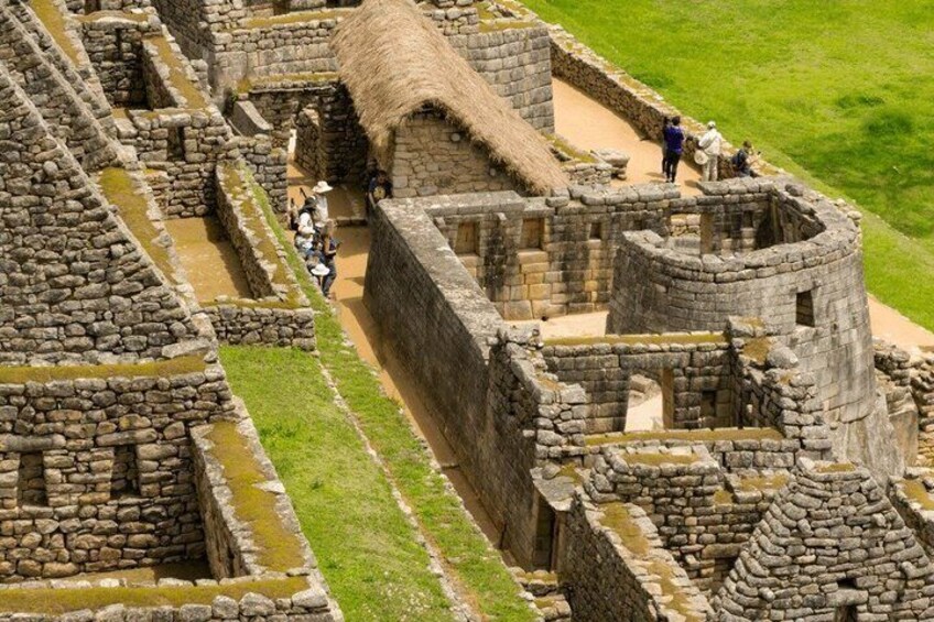Ancient stone ruins with a thatched-roof structure and visitors exploring the site. 3